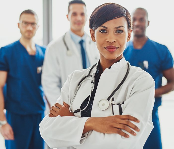 Black female doctor in front of team, looking at camera with medical team in background