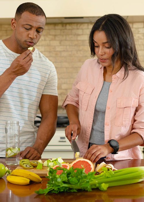 Young african american couple cooking together while eating at kitchen island. people, togetherness and cooking, unaltered.