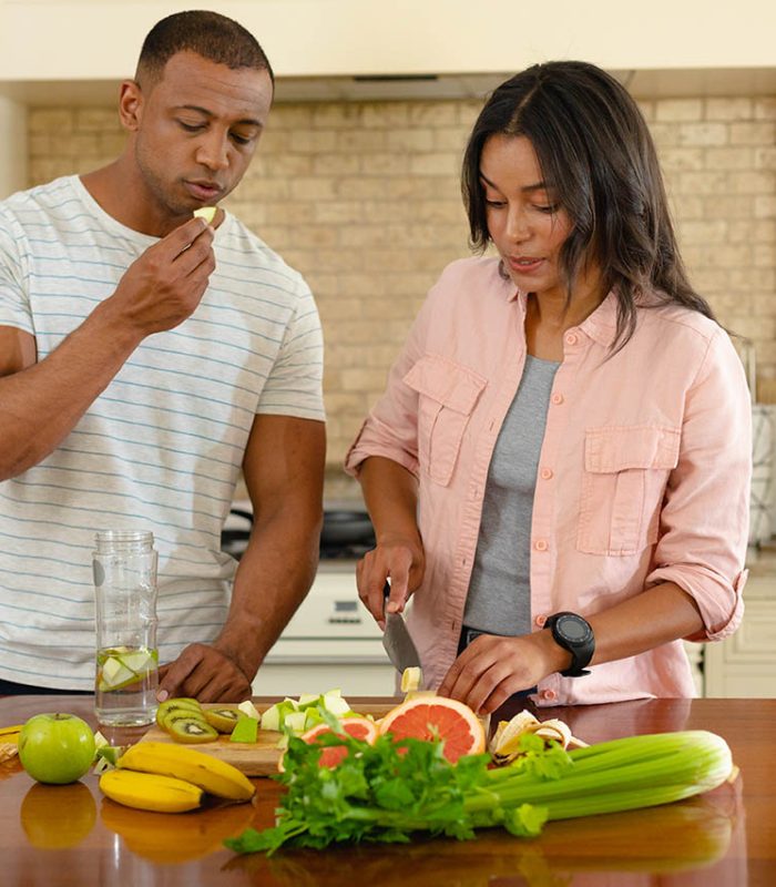 Young african american couple cooking together while eating at kitchen island. people, togetherness and cooking, unaltered.